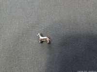 View of Pandora sterling silver dog charm from the side on a black fabric background, showing detailed silhouette of the dog's body, legs, and tail.
