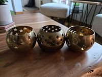 Front view of three brass tealight holders showing star, clover, and swirl cutouts with original patina.