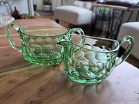 Photo showing the green glass creamer and sugar bowl on wooden table, highlighting honeycomb texture and shape.
