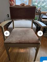 Front view showing cushioned backrest and seat, light hardwood frame and armrests, fabric shows some wear