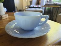 Angled side view of light blue teacup set on matching saucer with visible pie crust edging detail.
