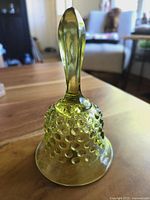 Side profile of the olive green hobnail glass bell with smooth handle and hobnail texture on bell body.