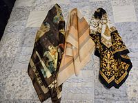 Three scarves laid out on a quilted bedspread showing varied colors and patterns: dark multicolored, beige striped, and black and gold ornate.