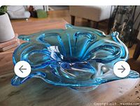 Top angle view showing the open, petal-like organic shape and ruffled edges of the blue glass dish on wood surface.