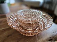 Stacked view of one large and four smaller pink depression glass bowls showing scalloped edge and glass texture
