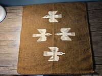 Front view of the rectangular brown Kelim tapestry with white bird pattern, showing textured handwoven fabric and edges.