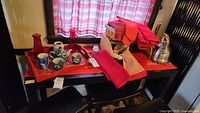 View of various kitchenware items on and around a table including red tray, tea set, towels, kettle, and bread box