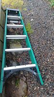 Top view of green metal ladder laid on gravel/moss ground showing metal steps and black end caps.