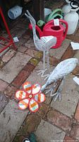 Front view showing two metal crane sculptures and a colorful pinwheel flower on a brick and concrete surface.