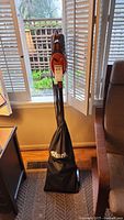Front view of upright Shark Rocket vacuum cleaner with orange handle and black fabric dust bag, standing indoors near a window
