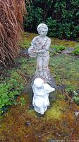 Two weathered garden statues placed on moss-covered ground, showing front and top down view.