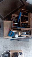 Overview of wooden saw horses and various hand tools including hand saw, hammer, hand drill, and clamps on carpeted floor.