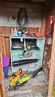 Shelf with various tools including two skill saws, sander, drill and extension cord hanging near the shelf