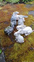 Top view of several weathered concrete yard statues of rabbits and a squirrel placed on mossy ground.