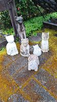 Overall view of six cat statues arranged on ground showing sizes, wear and weathering.