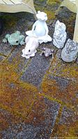 Full view of six frog and owl garden statues arranged on ground with mossy, grassy surface.