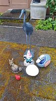 Front view of all six yard art pieces arranged on a mossy ground surface including tall bird, gnome, football, red bird, snail, and horned figurine.