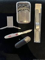 All items laid out: hand warmer, cutter, belt clip, pocket knife with sheath, packaged watch band