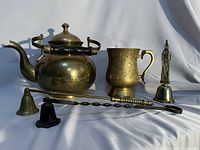 Group shot of brass tea kettle, mug, bells, and long snuffer