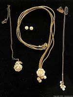 Overview of three necklaces and earrings laid on black background