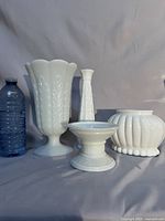 Group shot of four white milk glass pieces beside water bottle for scale
