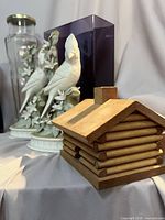 Lot overview showing wooden cabin, two porcelain cardinal figurines, tall clear vase, purple vase