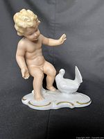 Front view of porcelain figurine showing nude child and dove on gold-trimmed base