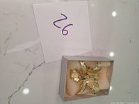 Gold tone flower brooch in a box with white padding, photo taken to show overall condition and presentation of the item