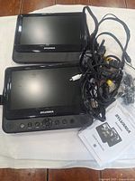 Two Sylvania car DVD player screens stacked with connected cables and user manual on a white surface.