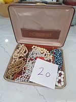 Open jewelry box showing assorted costume jewelry pieces including necklaces and bracelets in pearl-like and bead designs of various colors.