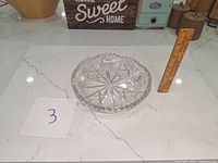 Photo of a clear round crystal dish with starburst and fan cut designs, standing next to a ruler for scale on a white countertop.