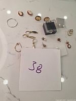 Photo of assorted earrings including cameo studs, gold-tone hoops, drop earrings with pearls, and other mixed styles on a countertop.