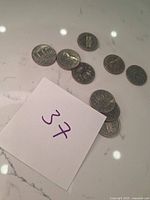 Top view photo showing nine Canadian fifty cent coins scattered on a marble-like surface with a paper showing the number 37.