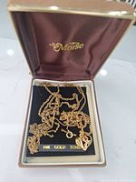 Moise jewelry box open showing three tangled 18K gold-tone chains and heart pendant on black insert