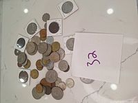 Top view of various international coins spread out on a white surface, some loose and some in white cardboard coin holders with clear windows.