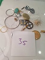 Various assorted jewelry items including bracelets, brooches, earrings and pendants arranged on a white surface.