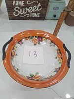 Top view of the vintage Noritake hand painted ceramic bowl showing floral design on white base with orange rim and black handles, note visible chips near handles.