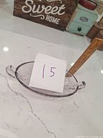 Clear oval glass serving dish with two small handles on a white countertop with wooden ruler measuring height