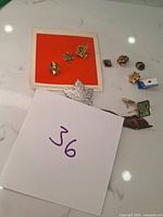 Pins spread on a surface, includes silver maple leaf and three gold-tone pins on orange card