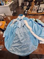 Front view of light blue glittery princess dress with matching blue hooded cape trimmed in white fur laid on table