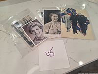 Multiple Royal family postcards placed on marble surface with handwritten '45' note, some in clear plastic sleeves.