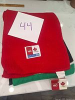 Folded red knit scarf with visible green and black knit sections, showing Olympic and HBC tags on top