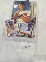 Three sports cards displayed on top of a plastic container filled with more cards. Cards feature Cal Ripken Jr., a New York Mets player, and a hockey player.