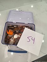Open metal tin filled with various U.S. coins and an orange plastic elephant figurine on top.