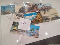 Eight vintage postcards spread on a white marble surface with a '49' note, showing various scenic and urban views in color and black and white.
