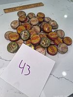 Top-down photo showing 43 assorted vintage soda bottle caps scattered on a white surface with a ruler for scale.