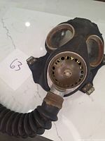 Front view of vintage gas mask showing circular metal filter and rubber hose attached.