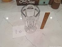 Clear glass goblet with scalloped rim and side handles next to wooden ruler for scale