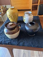 Four ceramic vases displayed on a black cloth on table, including the Roseville pottery crock and three decorative vases