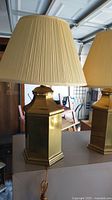Pair of large hexagonal brass plate table lamps with cream pleated shades, some brass marks visible.